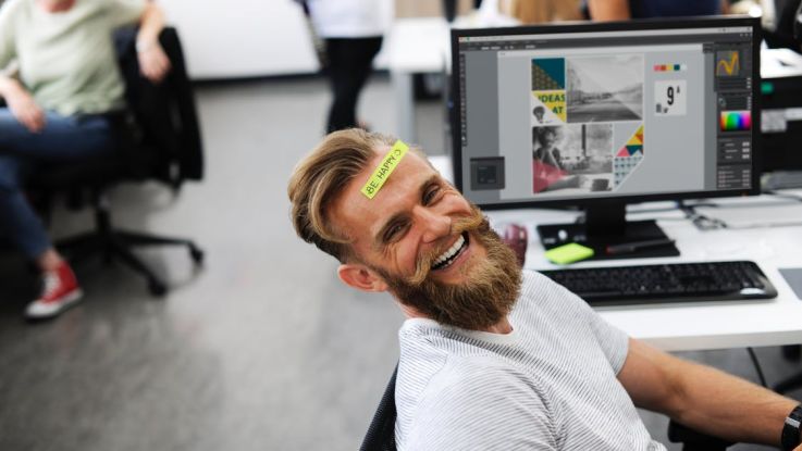 Lachender Mann an seinem Arbeitsplatz in einer Marketing Agentur